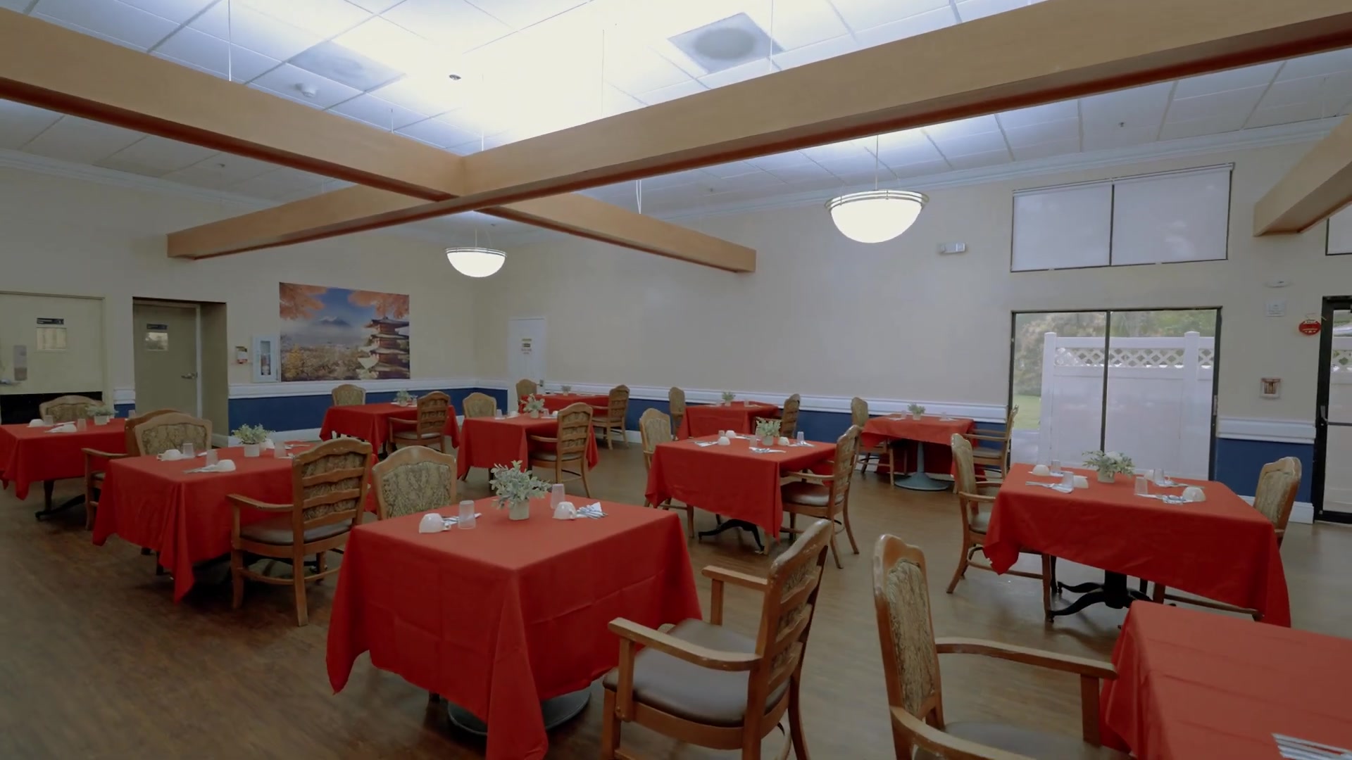 Restaurant-style dining room at Colonial Gardens senior care community in Lauderhill FL with red tablecloths and warm lighting